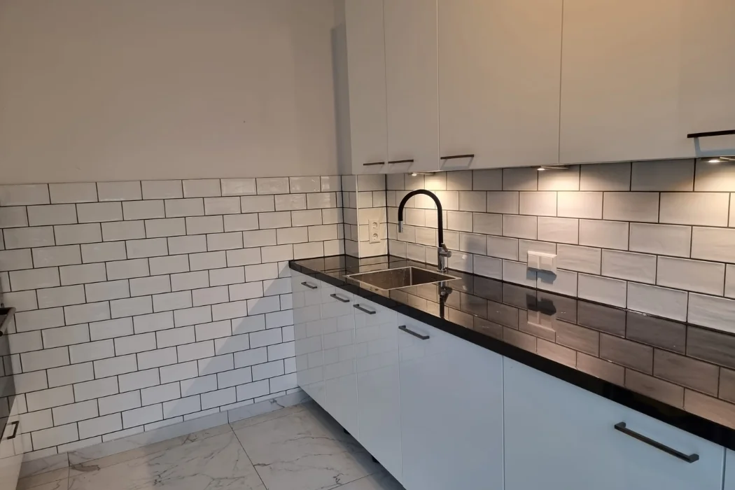 Keuken met witte kasten, lichte wandtegels en een donkere kraan en werkblad