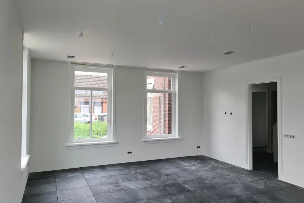 Binnenruimte met witte wanden en plafond, twee ramen en een betegelde vloer