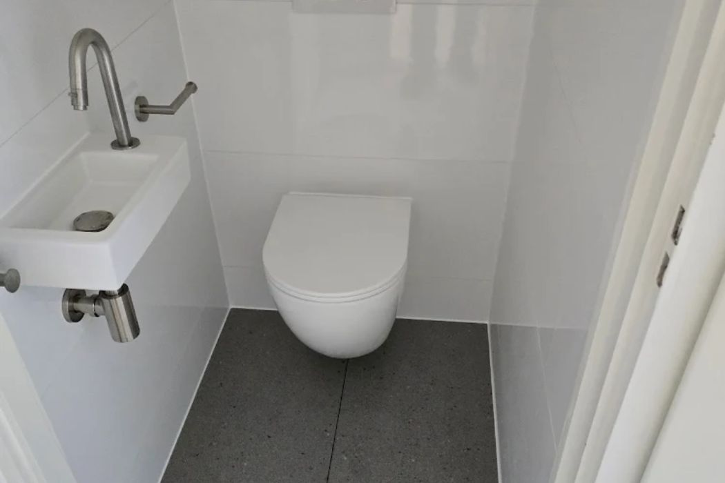 Compacte toiletruimte met wandcloset en een smalle witte wastafel