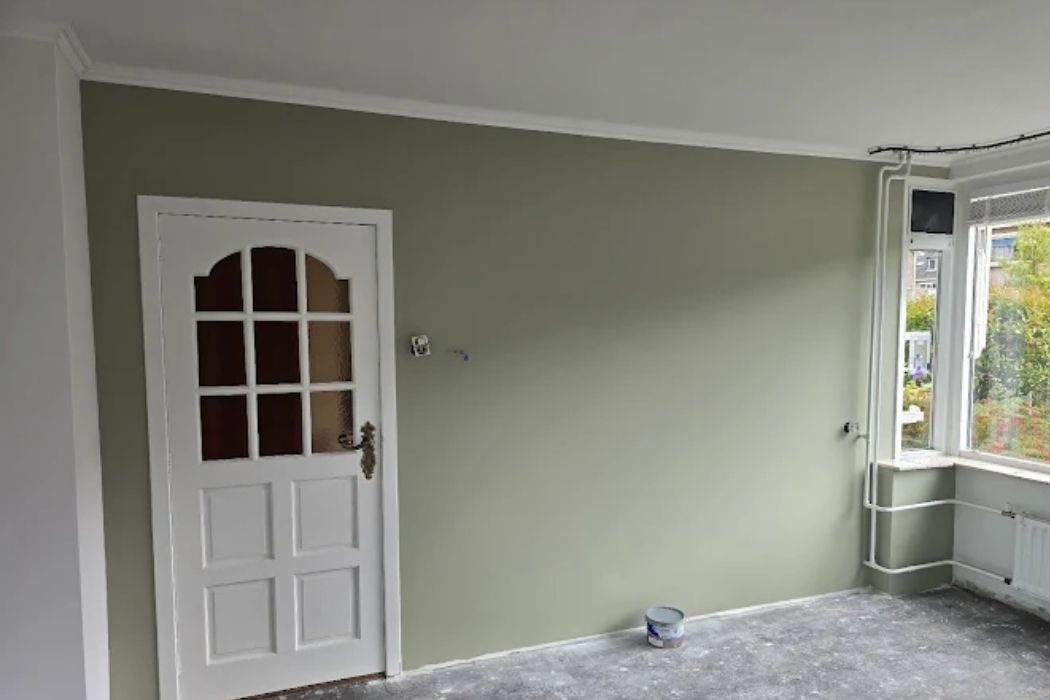 Woonkamer met geschilderde lichte groene wand en een nog onafgewerkte vloer