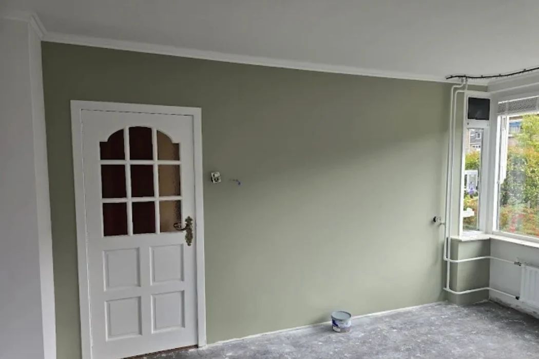 Woonkamer met geschilderde lichte groene wand en een nog onafgewerkte vloer